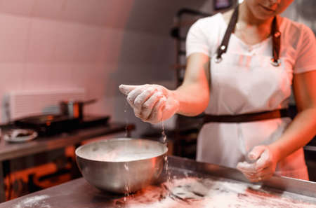 a female cook sprinkles flour on a metal table in the kitchen before making dough.の写真素材