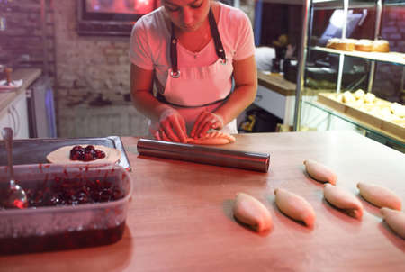the girl is a cook in the kitchen wrapping pies with cherry filling.の写真素材