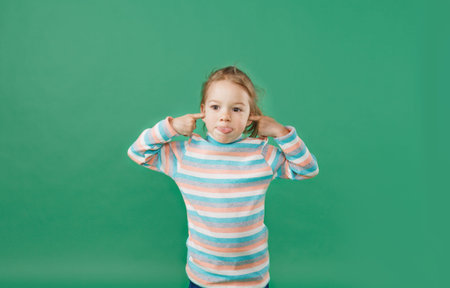 a little girl in a striped sweatshirt makes a face and shows her tongue on an isolated green...