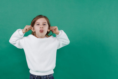 a boy with long hair makes faces, shows his tongue and holds his ears on a green isolated...