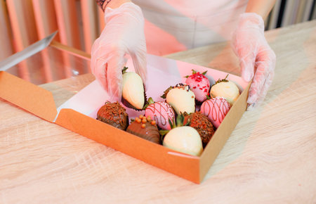 a pastry chef girl packs a large strawberry in chocolate into a box