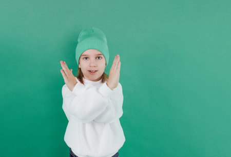 a boy in a white sweater and hat stands with his arms crossed in front of him on an isolated green...