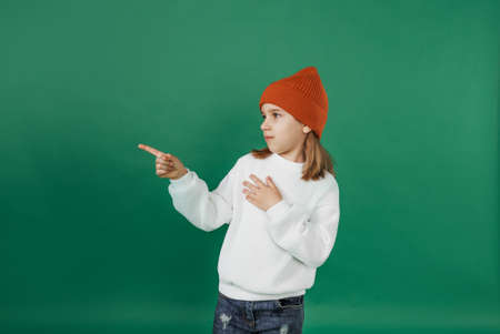 a handsome boy in a white sweater and hat shows and looks away on an isolated green background.の写真素材