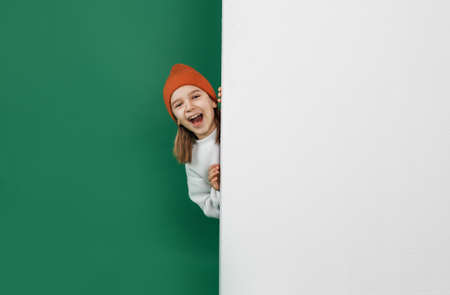 a little handsome boy hiding behind a white wall with an empty space, on an isolated green backgroundの写真素材