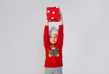 a little girl in a red pullover lifts a gift box up, joy is positive on an isolated white background.の写真素材