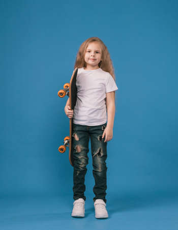 A stylish little girl learns to ride a skateboard on a blue background.の写真素材