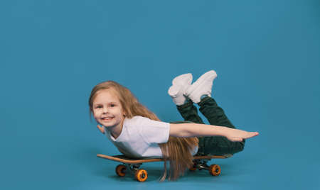 A stylish little girl learns to ride a skateboard on a blue background.の写真素材