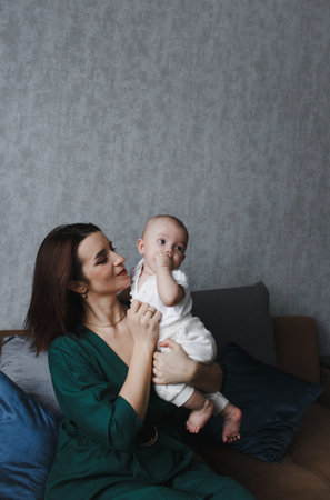A young tender happy mother hugs her newborn baby, smiling while sitting on the couch
