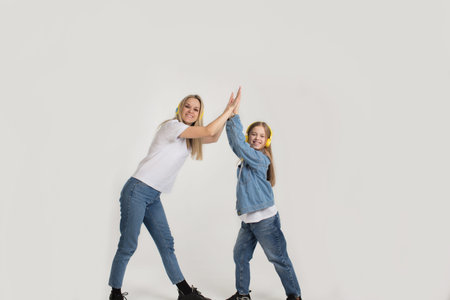 a woman and her daughter are dancing in yellow headphones on a white isolated background.