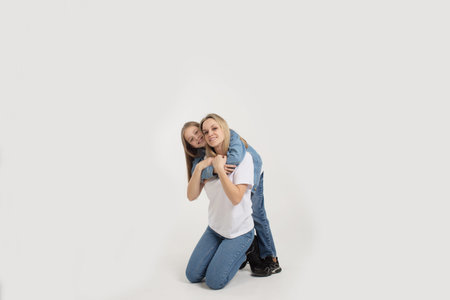 A beautiful young woman with her cute little daughter sitting on a white background.