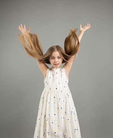 A beautiful girl in a light dress throws her hair up on a gray isolated background.の写真素材