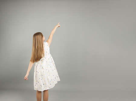Rear view of a little girl pointing up with my hand. Isolated on a gray background.の写真素材