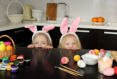 children in rabbit ears peek out from under the table against the background of the Easter decor....