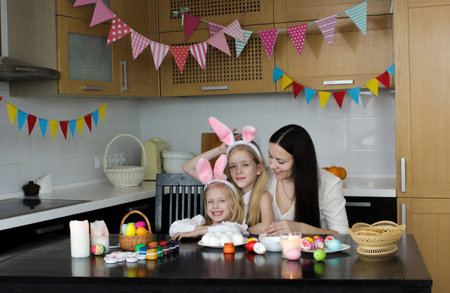 Mom and two little daughters draw Easter eggs. A happy family is preparing for Easter. Cute little...