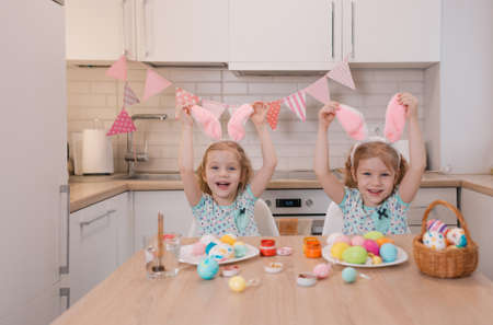 two little twin girls touch the rabbit ears on their heads with their hands while preparing for the Easter holiday. they laugh merrily.の写真素材