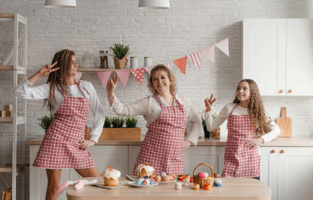 Mom and her daughter girls are dancing in the kitchen in aprons preparing for the Easter feast. Family vacation and unity.の写真素材