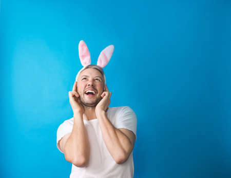 A gay man with makeup in a white T-shirt on a blue background holds rabbit ears in his hands looking at the camera. The concept of LGBTの写真素材