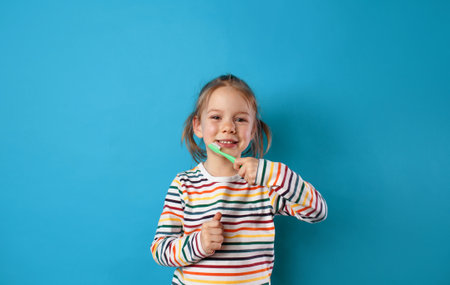 a happy little girl is brushing her teeth with a toothbrush on a blue isolated background.の写真素材