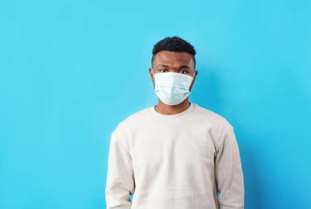 a young African American man wears a medical mask on a blue isolated backgroundの写真素材