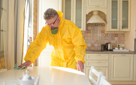 a man in a protective uniform wipes a table while cleaning an apartment