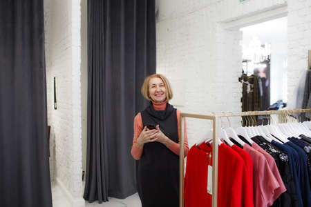 An adult woman chooses clothes on a hanger in the showroom of the store, smiling looking at the camera.の写真素材