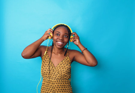 An African-American woman listens to music with yellow headphones on a blue backgroundの写真素材