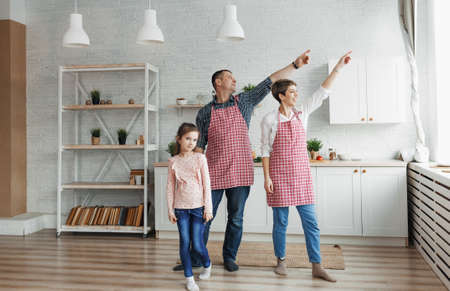 A cute girl watches her beautiful parents dance, everyone smiles, spending time together in the kitchenの写真素材