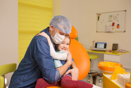 a male dentist hugs a little girl patient sitting in a dental chair.の写真素材