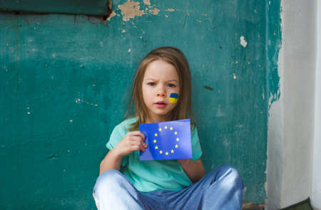 a little girl with a Ukrainian flag on her face holds the flag of the European Union in her hands. The war in Ukraine is the support of the European Union.の写真素材