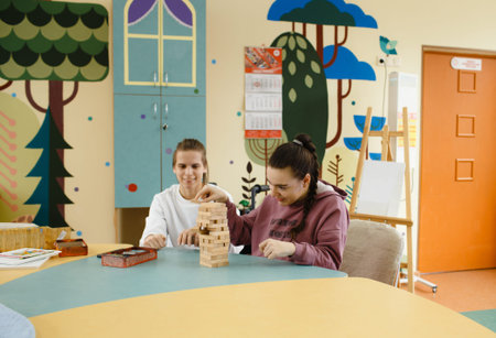 two girls with disabilities are playing jenga sitting at a large table.