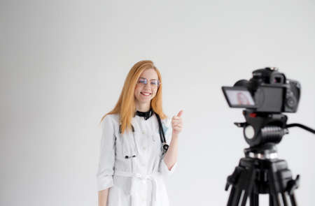Shooting for a medical video blog. A female doctor smiles and records a training video for her subscribers and patients. The doctor is a blogger. doctor online. telemedicine.の写真素材