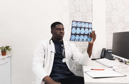 Close-up of an African-American doctor in a white coat looking at an X-ray image, CT, MRI,. Department of Radiologyの写真素材