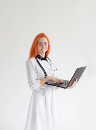 a doctor girl with red hair on a white background with a laptop in her handsの写真素材