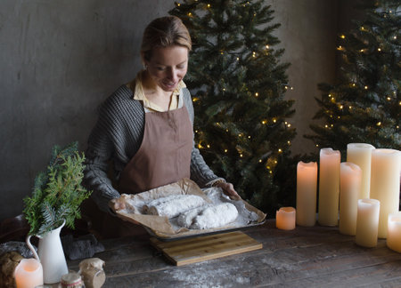A woman in a kitchen apron is preparing a Christmas stollen. A woman holds a pie on a wooden tray at Christmasの写真素材