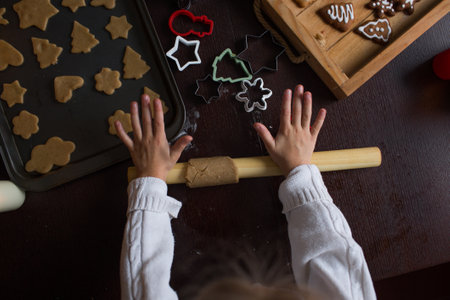 a little girl rolls out the dough with a rolling pin on the table and prepares Christmas cookies.の写真素材