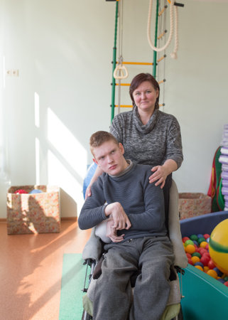 a boy with disabilities in a rehabilitation center with special needs next to his motherの写真素材