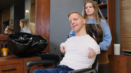 a man with disabilities in a white T-shirt does a haircut and hair styling in a barber shop. A full life for people with disabilities.の写真素材