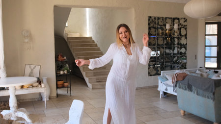 A joyful young woman is dancing in a bright modern living room.の写真素材