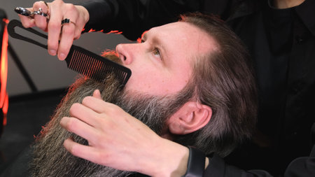 a hairdresser girl makes a beard styling for a man.の写真素材