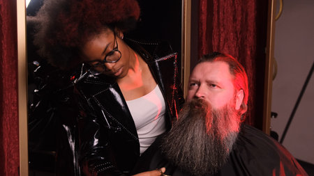 An African-American stylist girl is leveling a man's beard with scissors in a barber shop.の写真素材