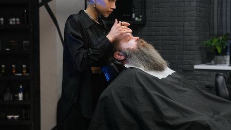 a stylist girl in a barbershop puts a moisturizer on the client's faceの写真素材