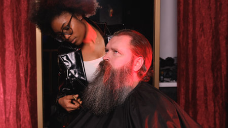 An African-American stylist girl is leveling a man's beard with scissors in a barber shop.の写真素材