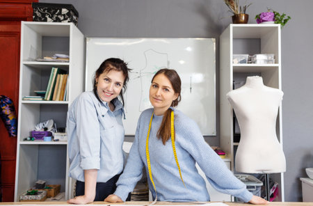 Two female fashion designers work together in a tailoring studio. A group of women dressmakers discusses fabric, pattern and sketch in a sewing workshop. The concept of small businessの写真素材