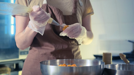 a female pastry chef in the kitchen fills custard cakes with butter cream using a pastry bag