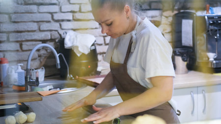 a woman in an open kitchen in a restaurant is rolling out dough with a rolling pin for making sausages in doughの写真素材