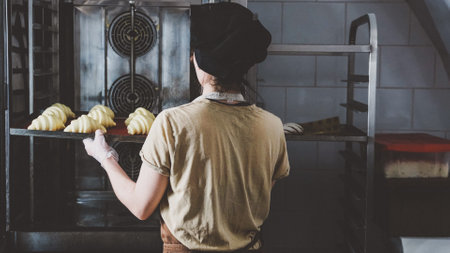 A working woman uses an oven to bake croissants Bakery concept.の写真素材