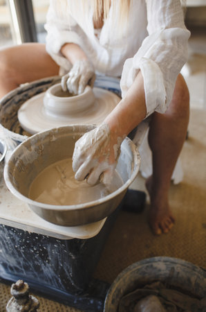 A woman works behind a potter's wheel. Creating handmade tableware.の写真素材