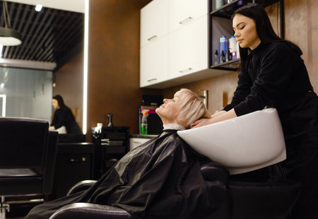 Portrait of an elderly woman visiting a professional hairdresser. An experienced hairdresser washes the client's hairの写真素材