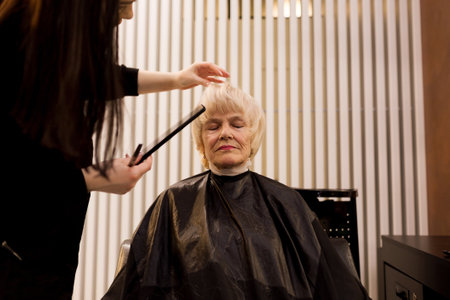 Portrait of an elderly woman visiting a professional hairdresser. An experienced hairdresser does hair styling for a clientの写真素材