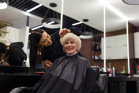 Portrait of an elderly woman visiting a professional hairdresser. An experienced hairdresser does hair styling for a clientの写真素材